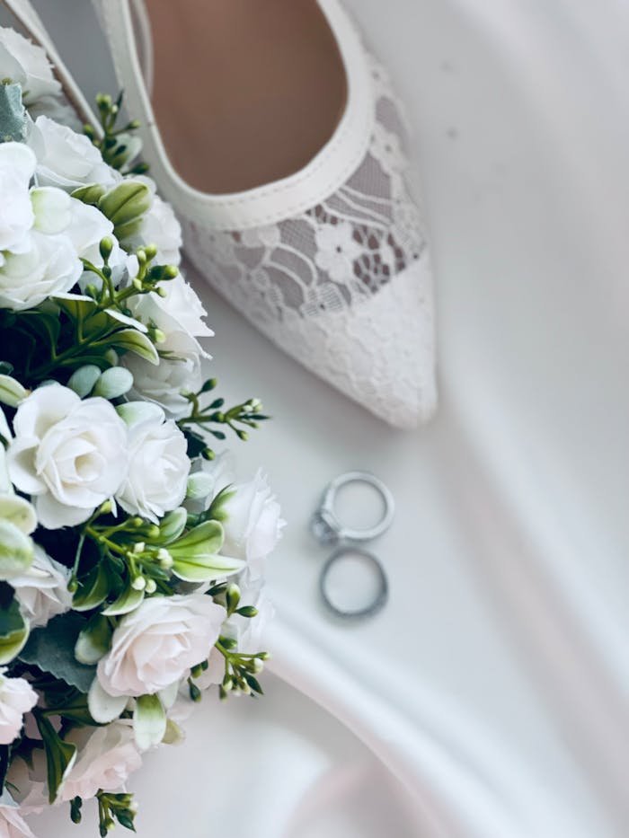 Elegant wedding setup featuring a white bouquet, lace shoe, and rings.