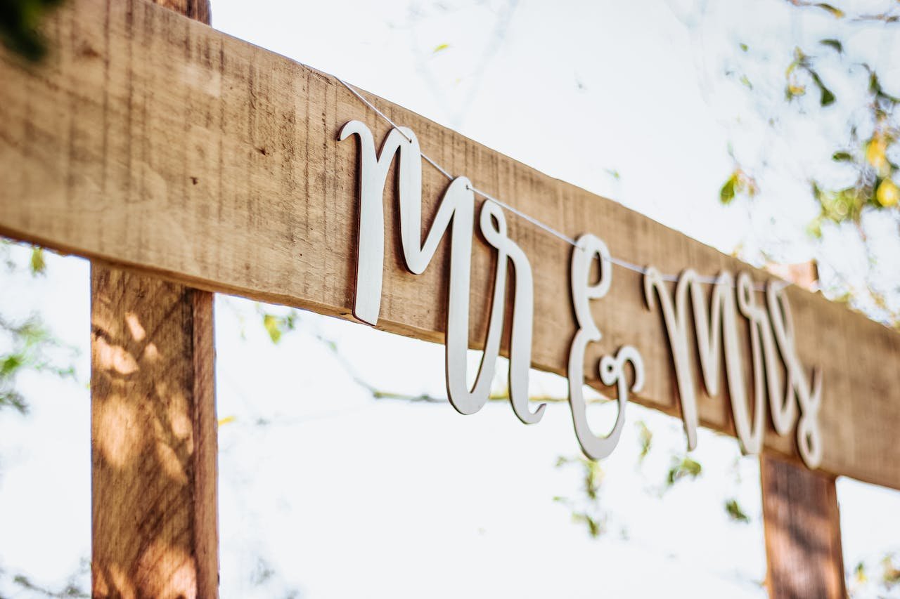services-04 A close-up of a rustic wooden wedding sign featuring 'Mr & Mrs' text on a sunny day.